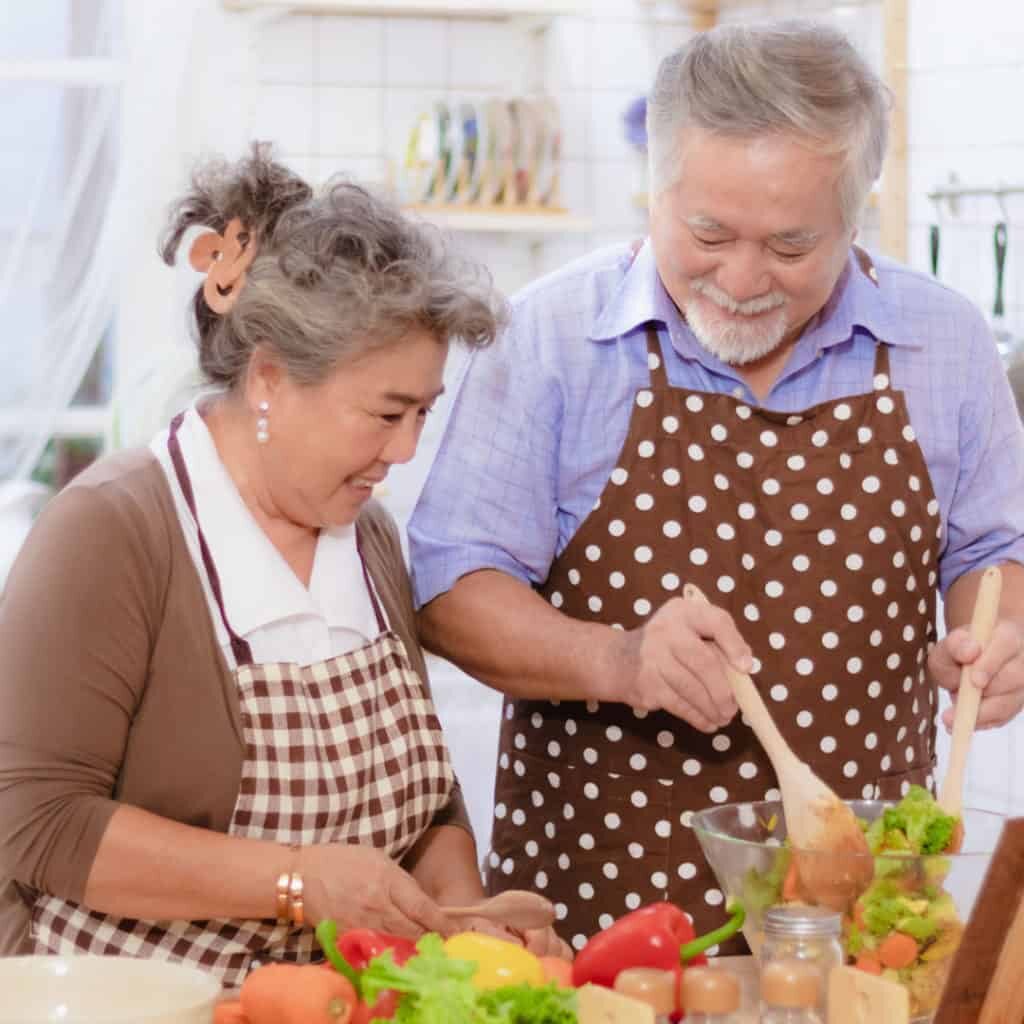 Square image of older couple preparing a salad